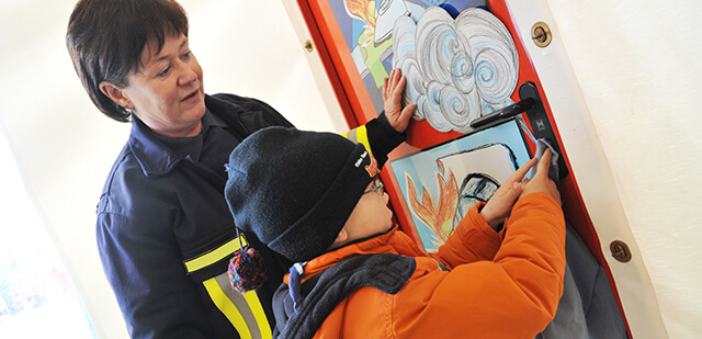 Eine Feuerwehr-Frau erklärt einem Jungen etwas zum Brandschutz.