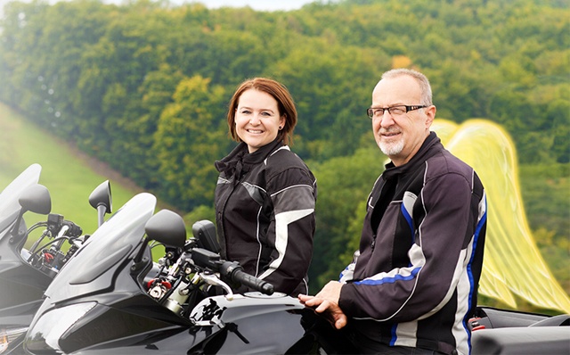 Motorradversicherung: Eine Frau und ein Mann sitzen jeweils auf einem Motorrad. Der Mann hat Schutzengel-Flügel.